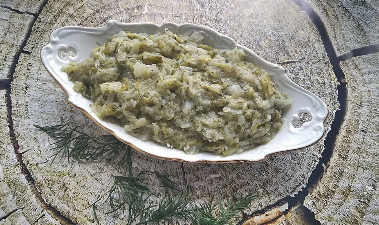 Pyszna kapusta zasmażana z koperkiem, podana w ozdobnej misie na tle drewnianej tekstury.