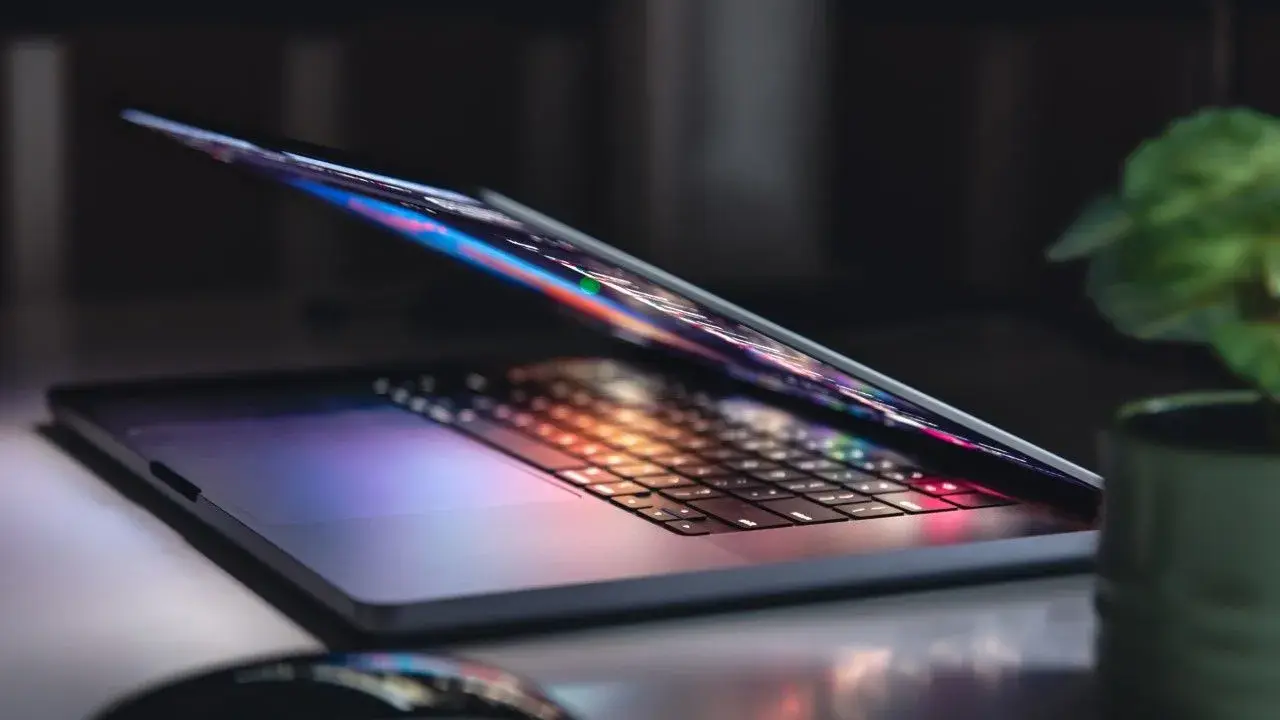 Otwarty notebook z podświetlaną klawiaturą i ekranem, obok myszka i roślina. To jest właśnie notebook, narzędzie do pracy i rozrywki.