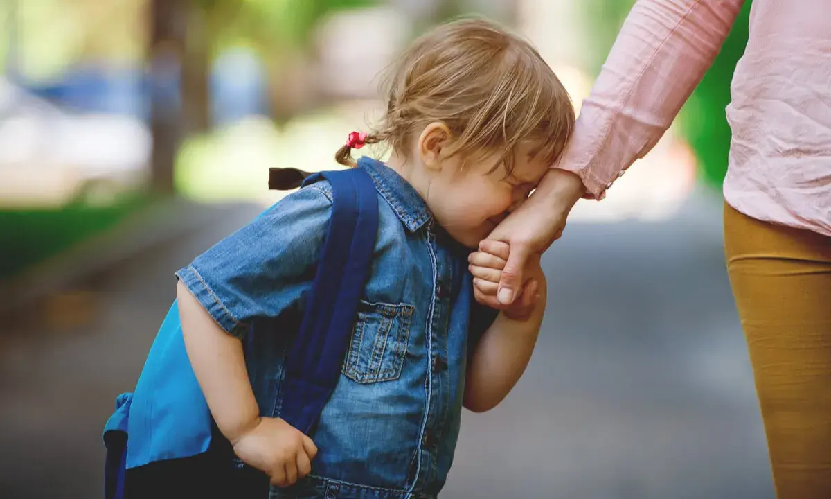 Niña con mochila azul llora y se aferra a la mano de su madre. Parece que mi hija no quiere ir al colegio.
