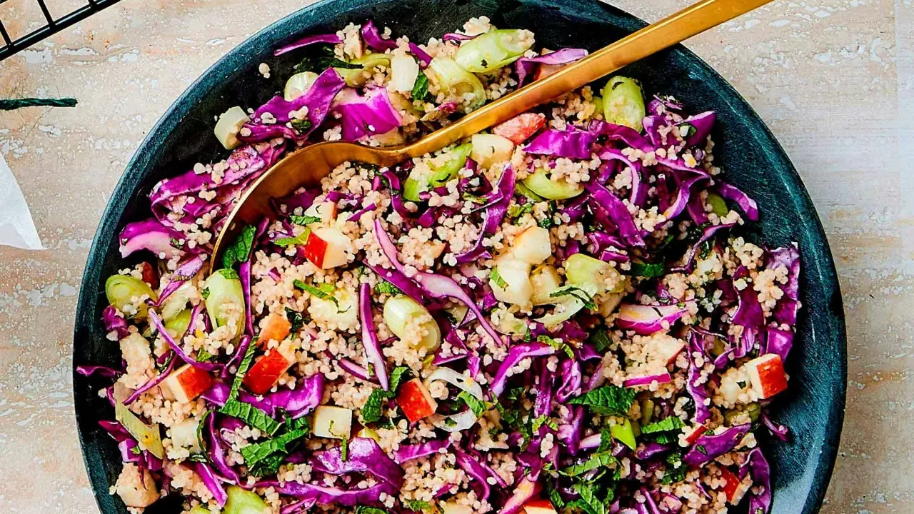 En färgglad couscous sallad med rödkål, äpple och mynta. En gyllene sked vilar i den fräscha rätten.