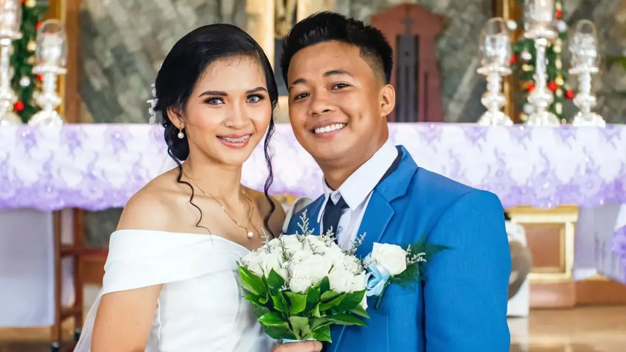 Novios sonriendo, ella con vestido blanco y él con traje azul. Un ramo de rosas blancas. Agradecimiento a los novios por la boda.