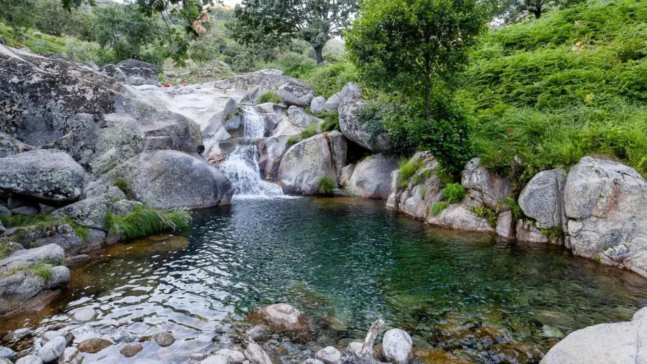Unas idílicas piscinas naturales en Valladolid, con cascadas y rocas, rodeadas de vegetación exuberante.