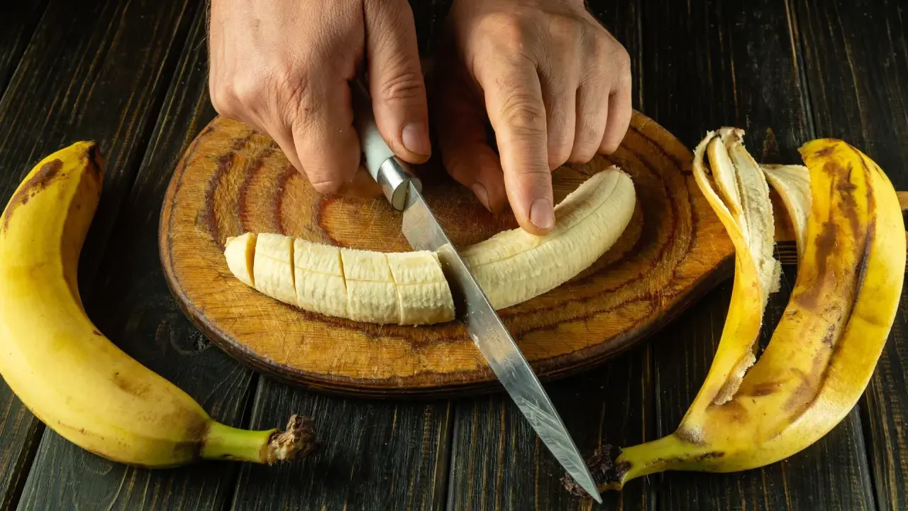 Dłonie kroją banana na desce. To świetny pomysł, co jeść na skurcze nóg, bo banany są bogate w potas.