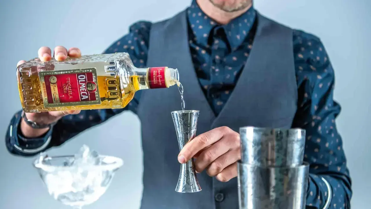 Barman nalewa Olmeca Tequila Gold do miarki, idealna tequila do margarity. Obok kieliszek z lodem i shaker.