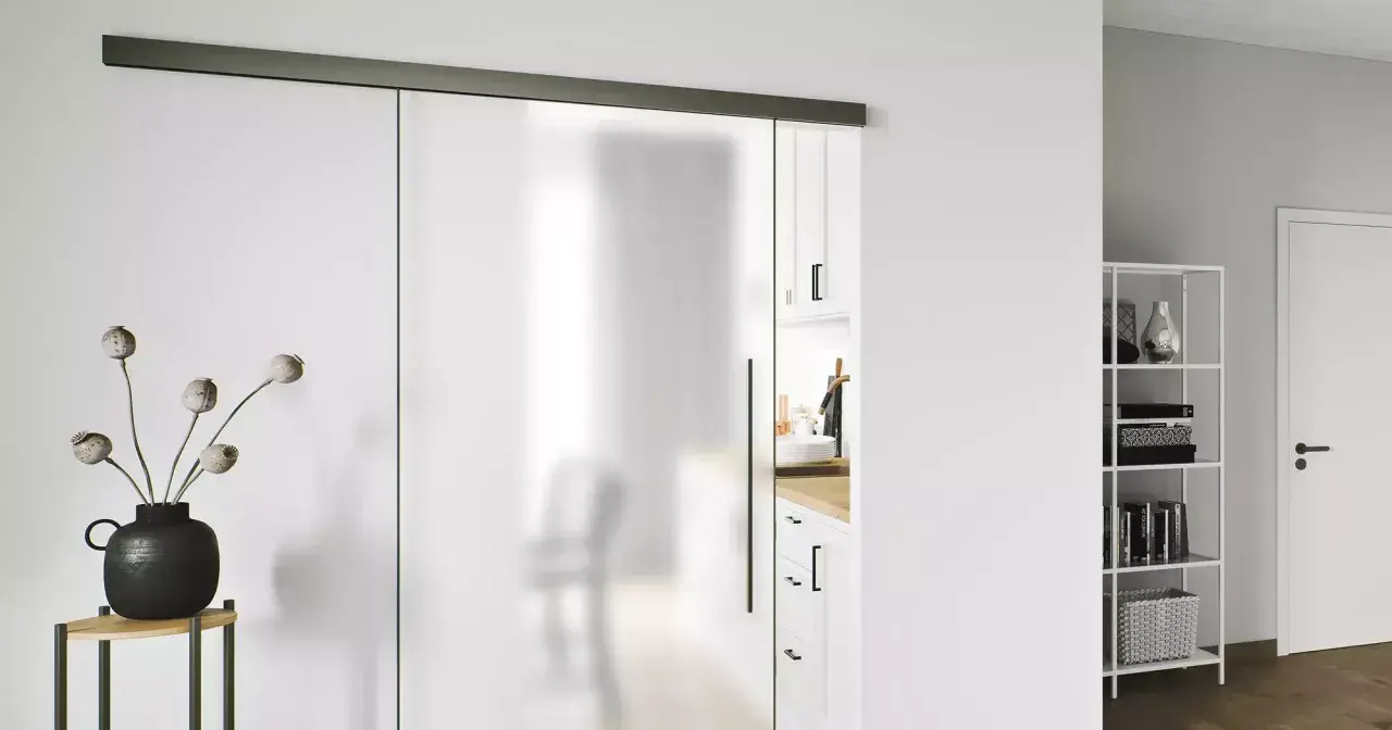Puerta corredera de cristal esmerilado con tirador negro. Una guía superior negra y un riel inferior negro son clave para como poner una puerta así.