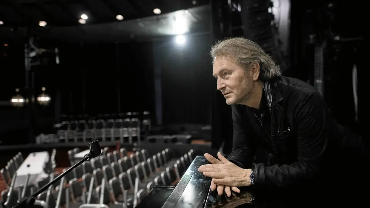 Tomas Ledin lutar sig mot en pianokant i en tom teatersalong, kanske förbereder han sig för Melodifestivalen.