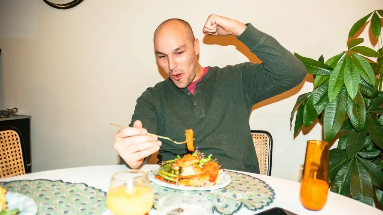 Mann feiert sein **Essen nach Marathon** mit einem kräftigen Bizeps-Zeigen und einem Bissen vom Teller.