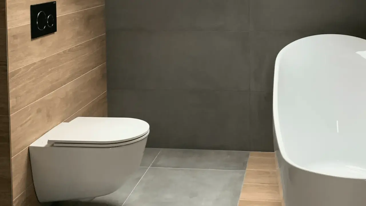 Salle de bain moderne avec un élégant **pose wc suspendu** sur un mur en bois, face à une baignoire blanche et des murs gris.