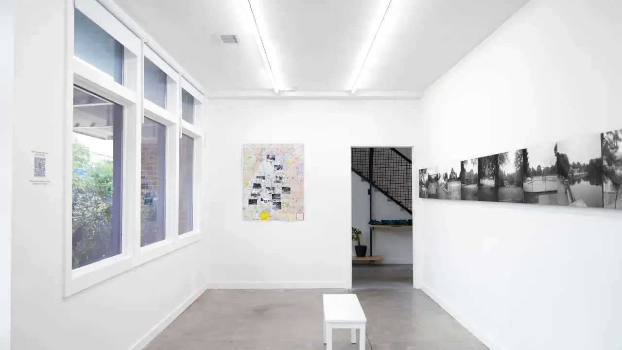 Inside the Atlanta Center for Photography, a white bench sits before a map artwork. Black and white photos line the opposite wall.