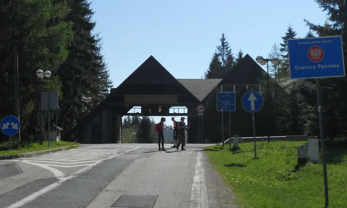 Przejście graniczne na Pilsku. Znaki drogowe i budynek z napisem "Wyciągi Narciarskie". Szlaki górskie w tle.