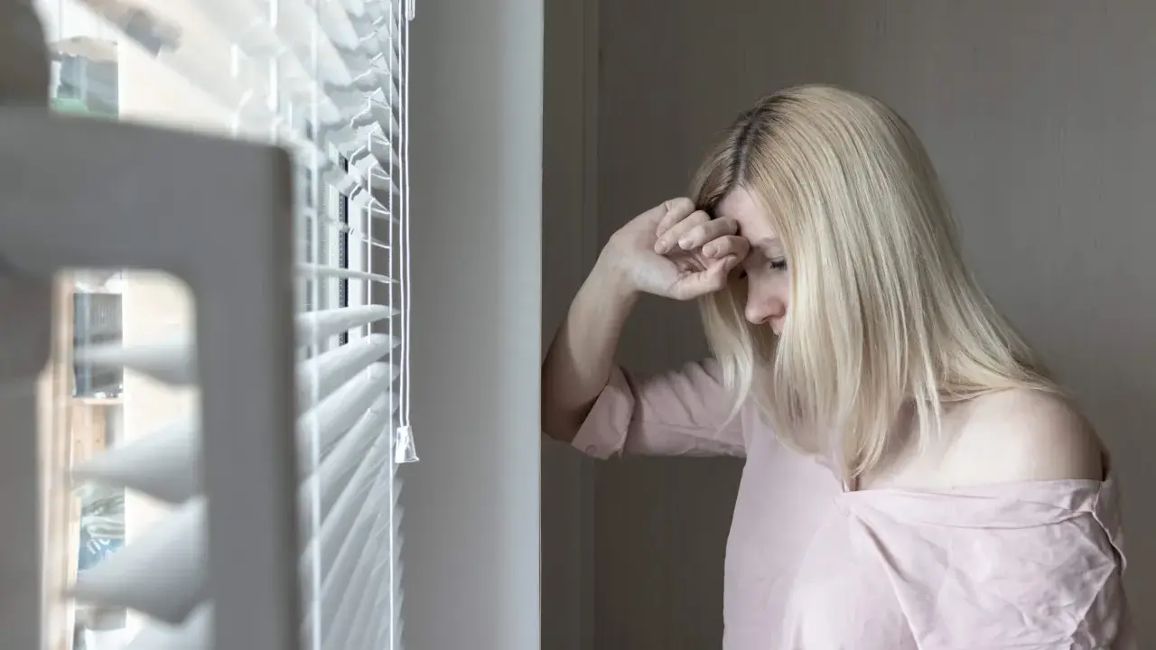 Mujer rubia con la mano en la frente, mirando hacia abajo, con un aire de melancolía que evoca el síndrome de Wendy.
