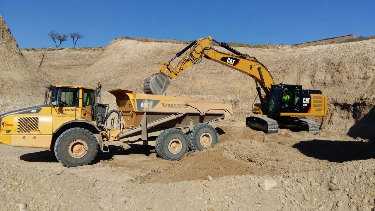 Excavadora CAT cargando volquete Volvo en obra de movimiento de tierras.