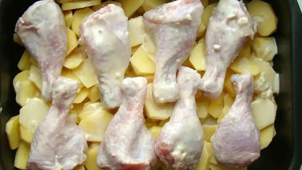 Osiem pałek kurczaka w sosie, ułożonych na plastrach ziemniaków w brytfannie. Idealne do pieczenia, by uzyskać chrupiące pałki z kurczaka w piekarniku.