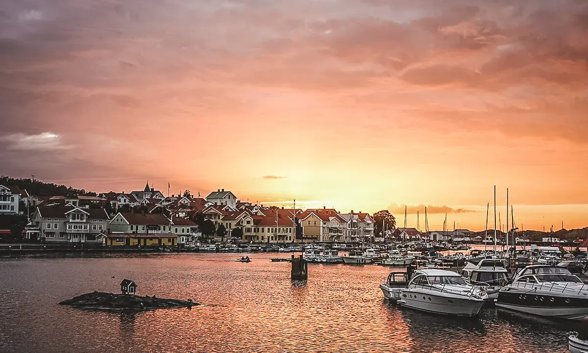En pittoresk svensk kuststad vid solnedgången, med båtar i hamnen och hus längs vattnet. En perfekt plats för upplevelser i Sverige.