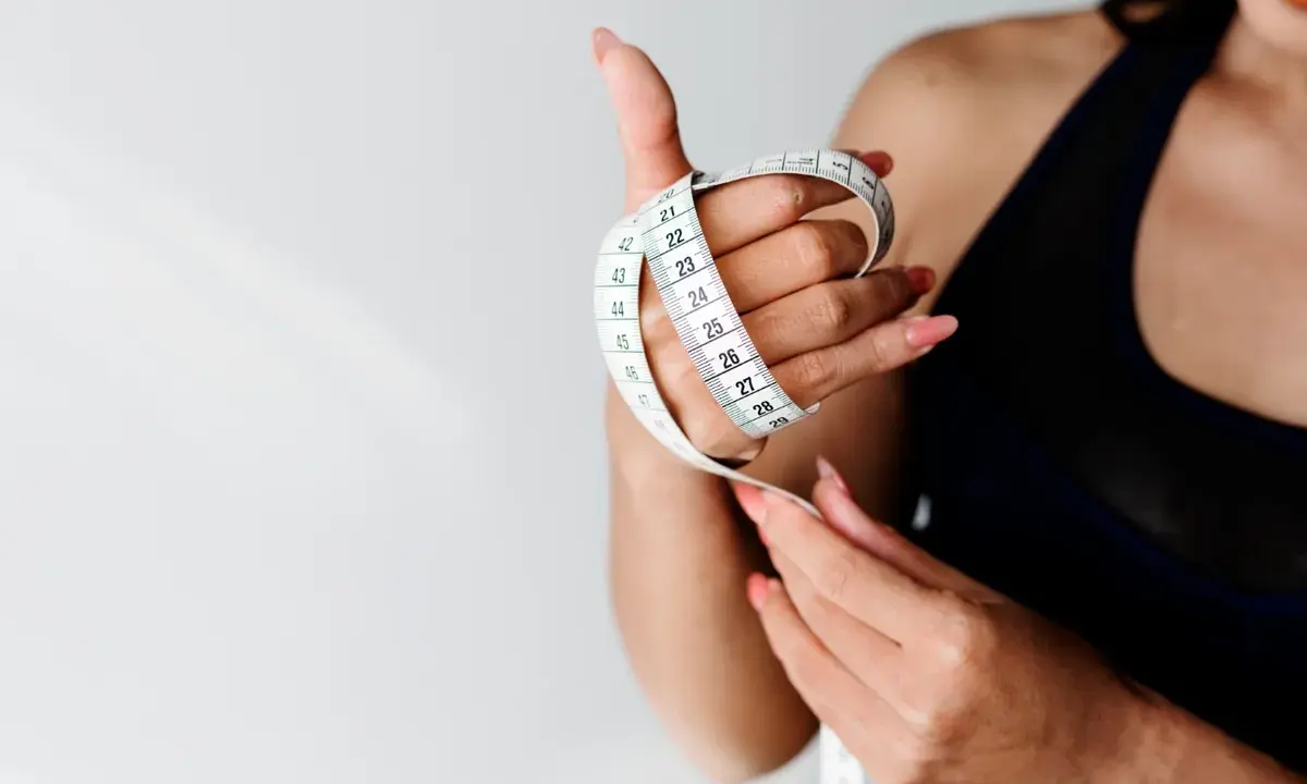 Kobieta z miarką w dłoni, symbolizującą kontrolę nad wagą i dążenie do idealnego BMI.