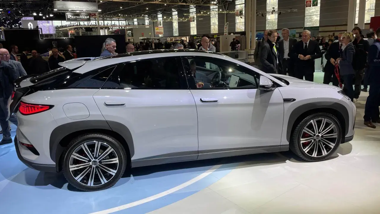 En vit BYD-bil visas på en mässa. Människor tittar på bilen, kanske potentiella byd återförsäljare.