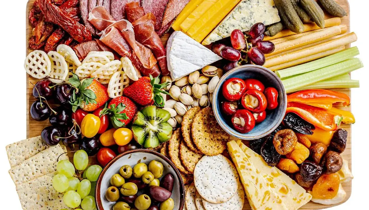 En generös bricka med kall mat: salami, skinka, ostar, oliver, frukt, grönsaker och kex. Perfekt för en festlig tillställning.