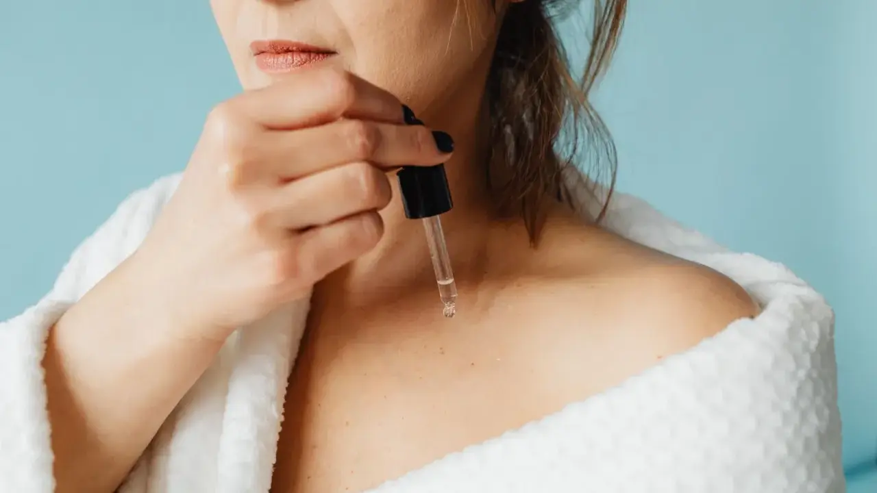 Une femme applique un sérum à base de peptide sur sa peau, enveloppée dans un peignoir blanc douillet.