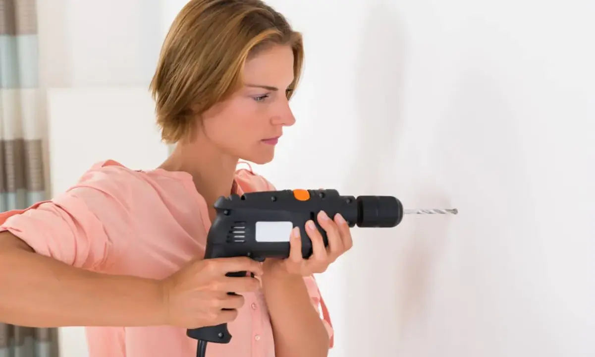 Mujer usando un taladro, mostrando sus partes como el gatillo y la broca, para hacer un agujero en la pared.