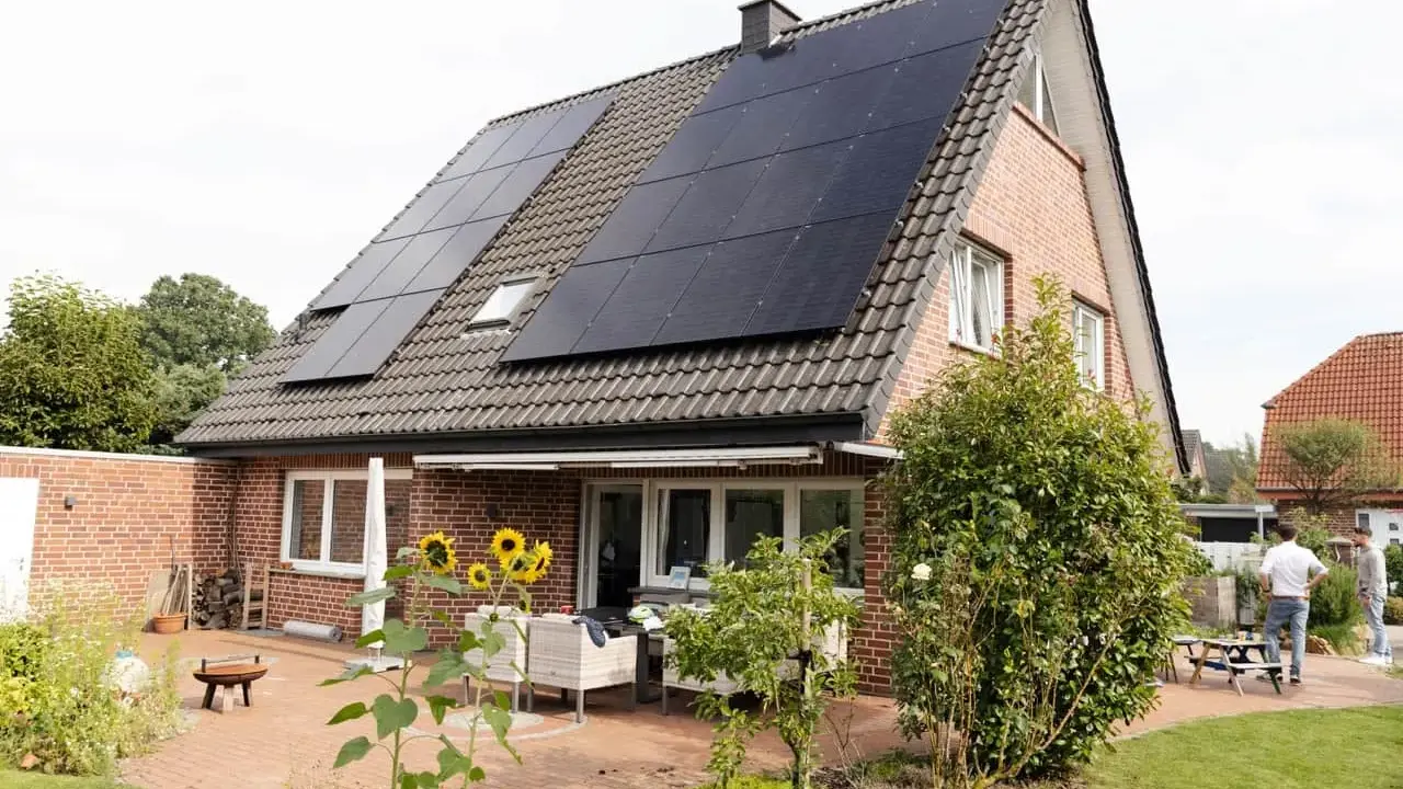 Tak på ett tegelhus med solceller som ger hög verkningsgrad. Solrosor blommar på uteplatsen.