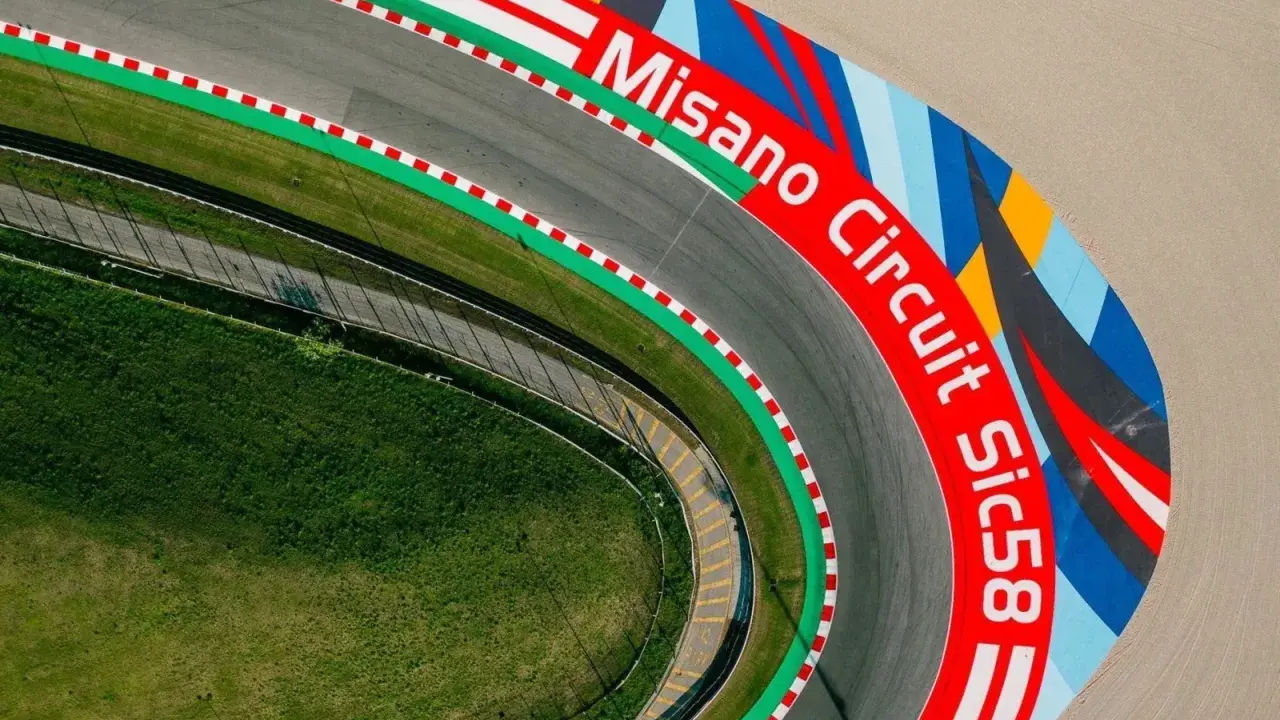 Vista aerea del circuito di Misano, con la scritta "Misano Circuit Sic58" in rosso e un disegno colorato.