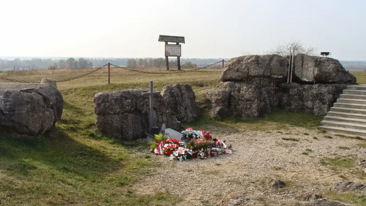 Pomnik na Górze Strękowej z krzyżem i wieńcami. W tle widoczne bunkry i krajobraz.