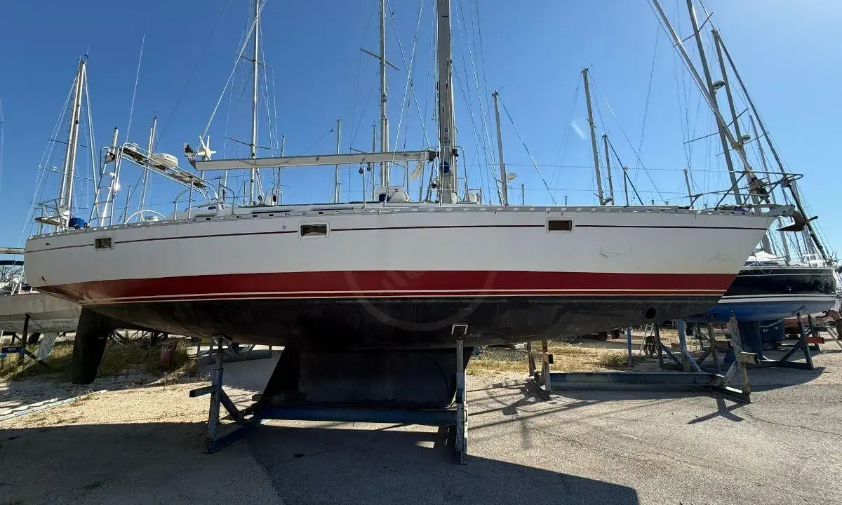 Un voilier blanc et rouge, prêt pour l'aventure, est exposé sur des bers. Ce navire, un modèle de **Gibert Marine**, attend de retrouver les flots.