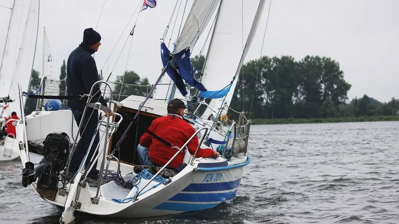 Deux hommes naviguent sur un voilier micro challenger, le vent gonflant les voiles sur un lac calme.