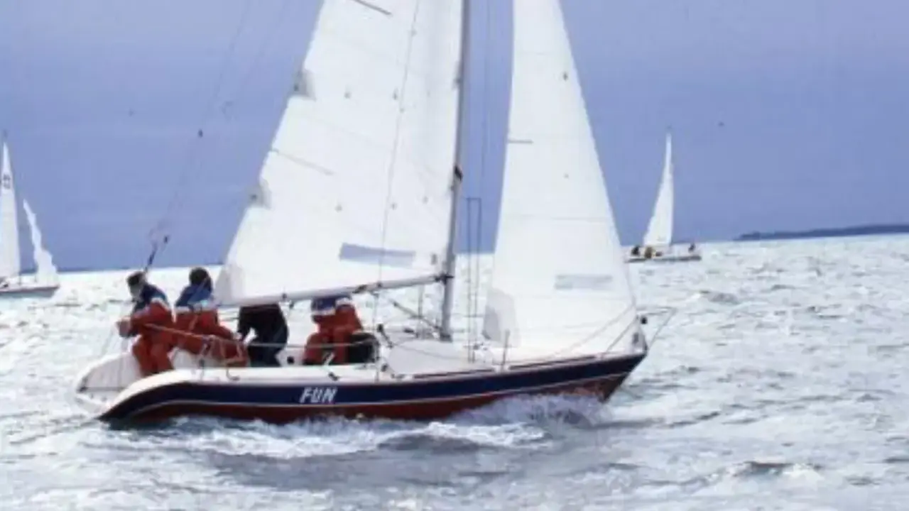 Un voilier nommé "FUN" navigue sur une mer agitée, avec des personnes à bord profitant de la navigation.
