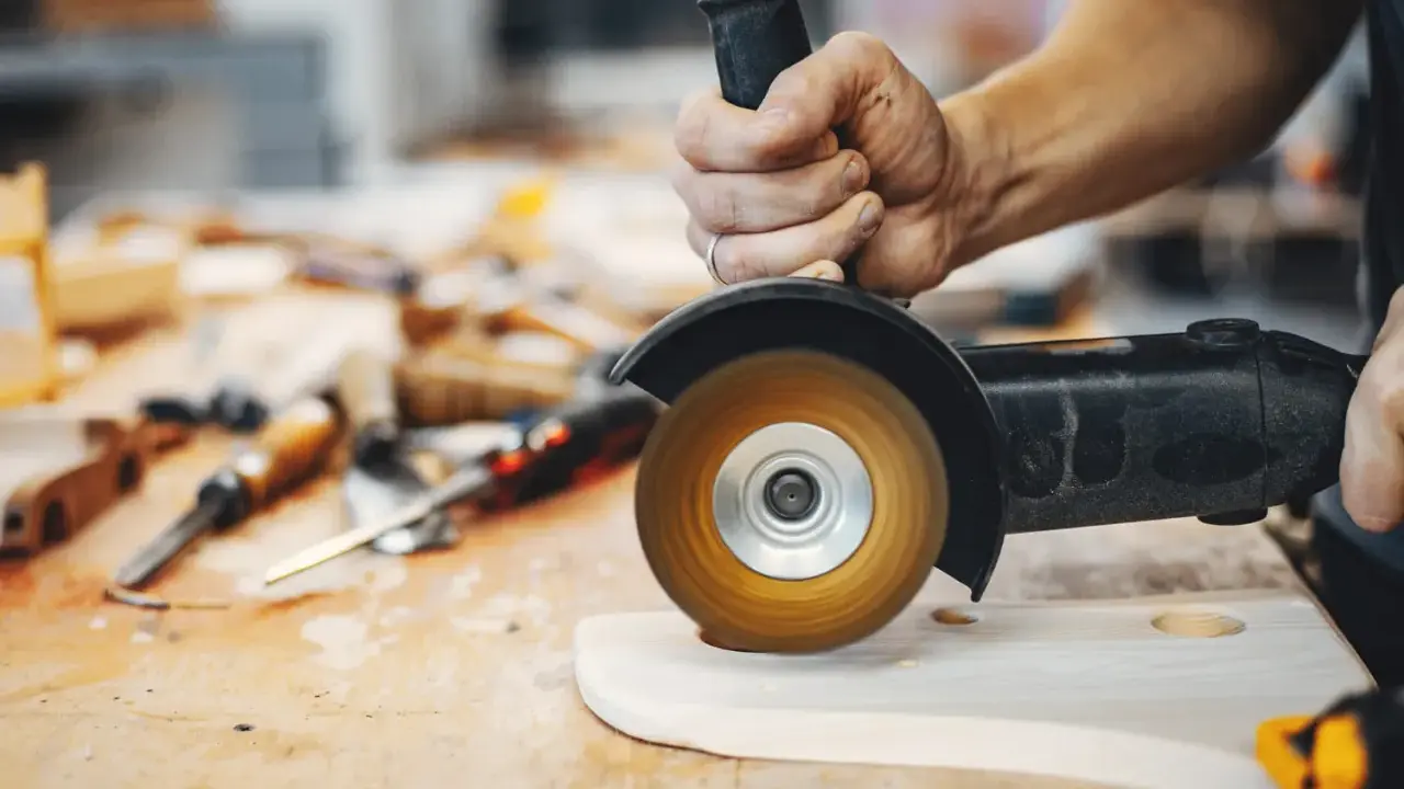Mano trabajando con amoladora, mostrando sus usos en carpintería para dar forma a la madera.
