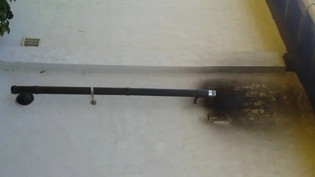 Tuyau d'évacuation noir d'un poêle à pellet ventouse, fixé au mur blanc, avec des traces de suie autour de la sortie.