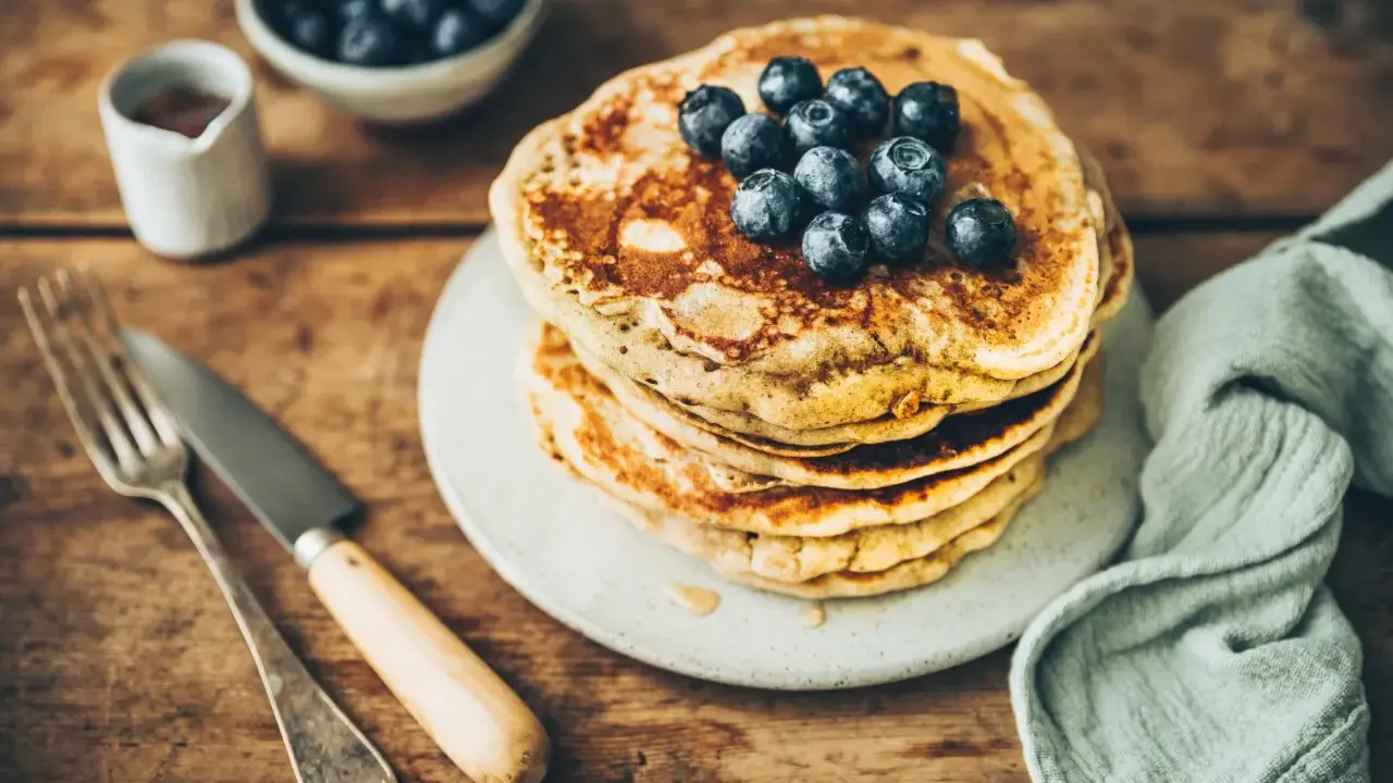 Pile de pancakes au levain garnis de myrtilles, sur une assiette, avec une fourchette et un couteau.