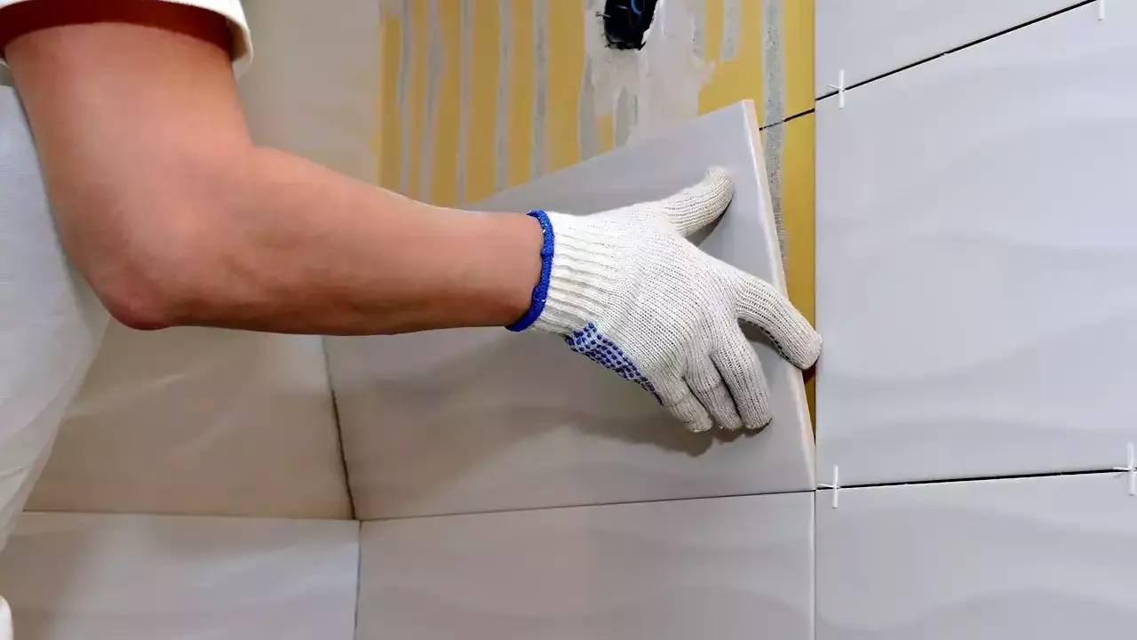 Man con guantes coloca una baldosa nueva sobre un alicatado existente.