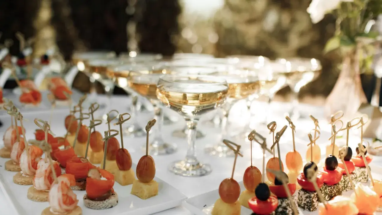 Elegantes aperitivos para bodas: camarones, salmón, queso y frutas en brochetas, junto a copas de champán.
