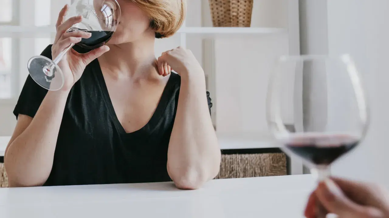 Kobieta z krótkimi blond włosami pije czerwone wino. Czy zastanawiasz się, jak hashimoto a alkohol wpływają na zdrowie?