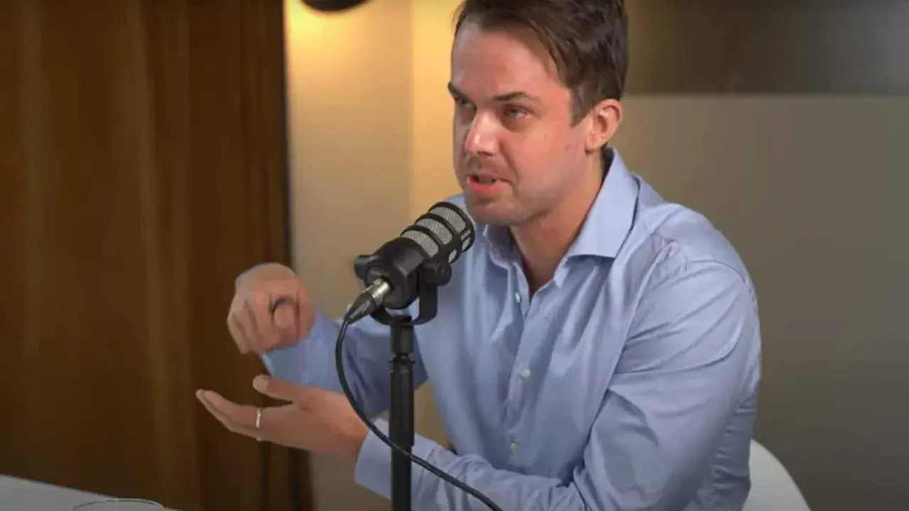 Michael van de Poppe w niebieskiej koszuli mówi do mikrofonu, gestykulując.