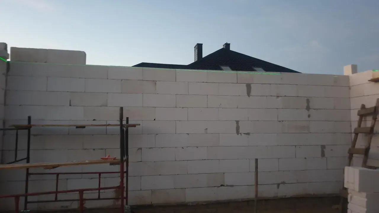 Budowa domu z bloczków, zielona linia laserowa wyznacza poziom. To dobry pomysł na krzywe ściany, jeśli chcesz uzyskać ciekawy efekt architektoniczny.