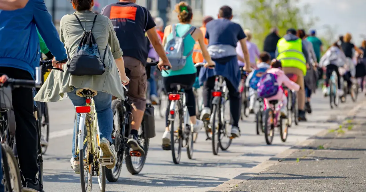 Grupa rowerzystów jedzie w kolumnie, przestrzegając przepisów. Widać plecaki i kamizelki odblaskowe.