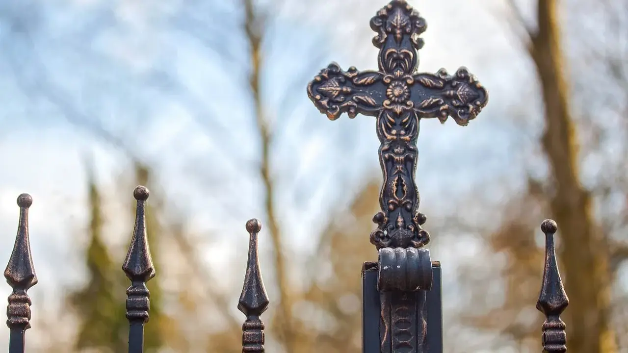 Krzyż na metalowym ogrodzeniu, symbol nadziei i walki z siedmioma grzechami głównymi.