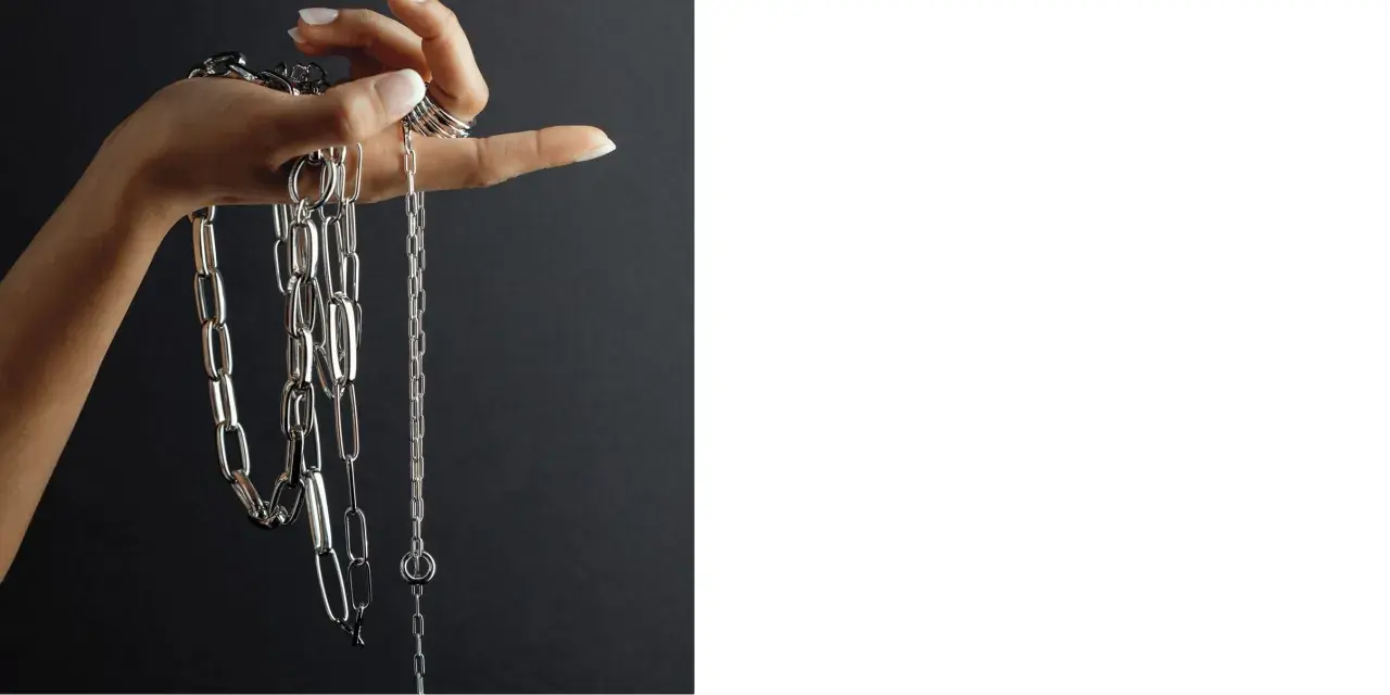 Mano con anelli che mostra diverse collane Pesavento, con maglie lucide e un design moderno. Scopri i prezzi.