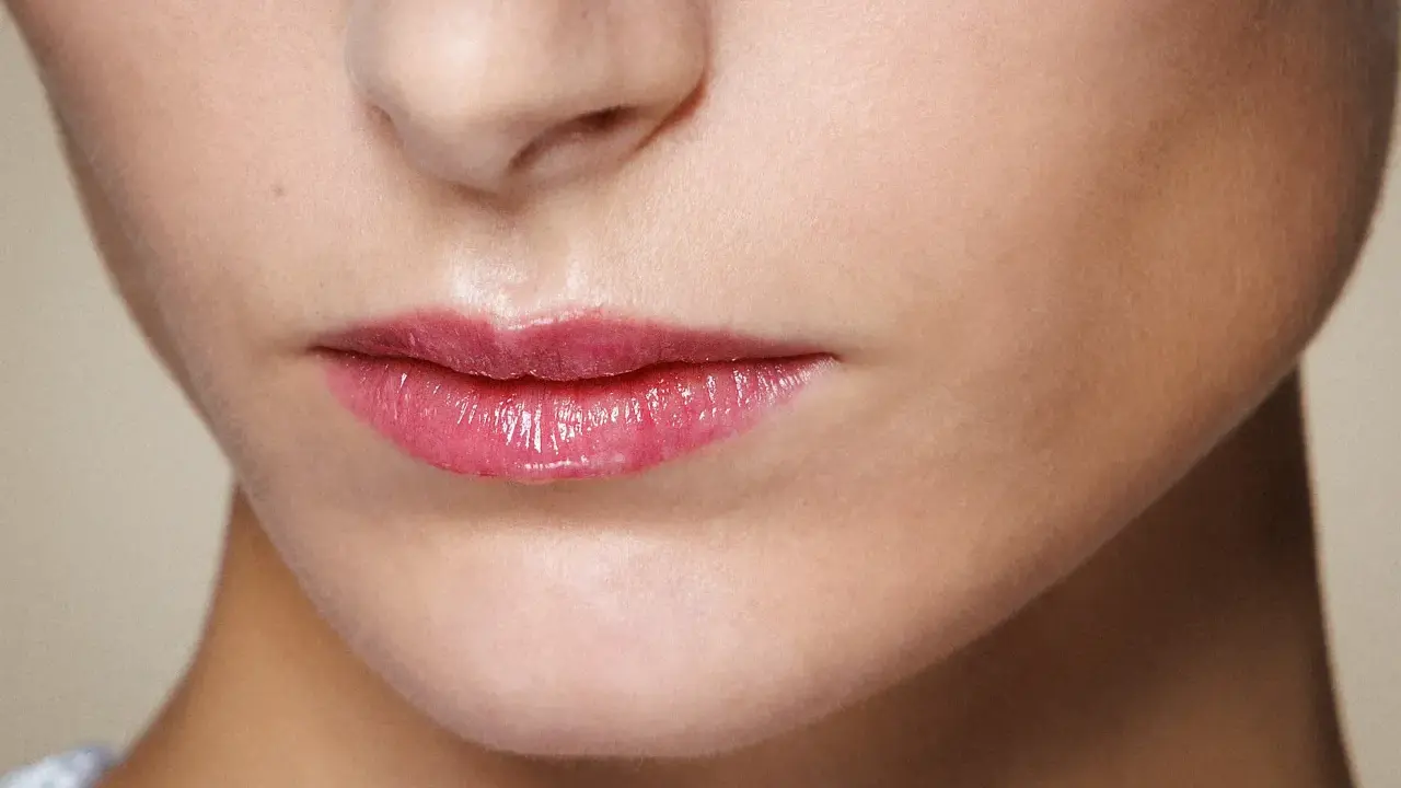 Labbra sottili e lucide con un tocco di gloss rosa, che catturano la luce.