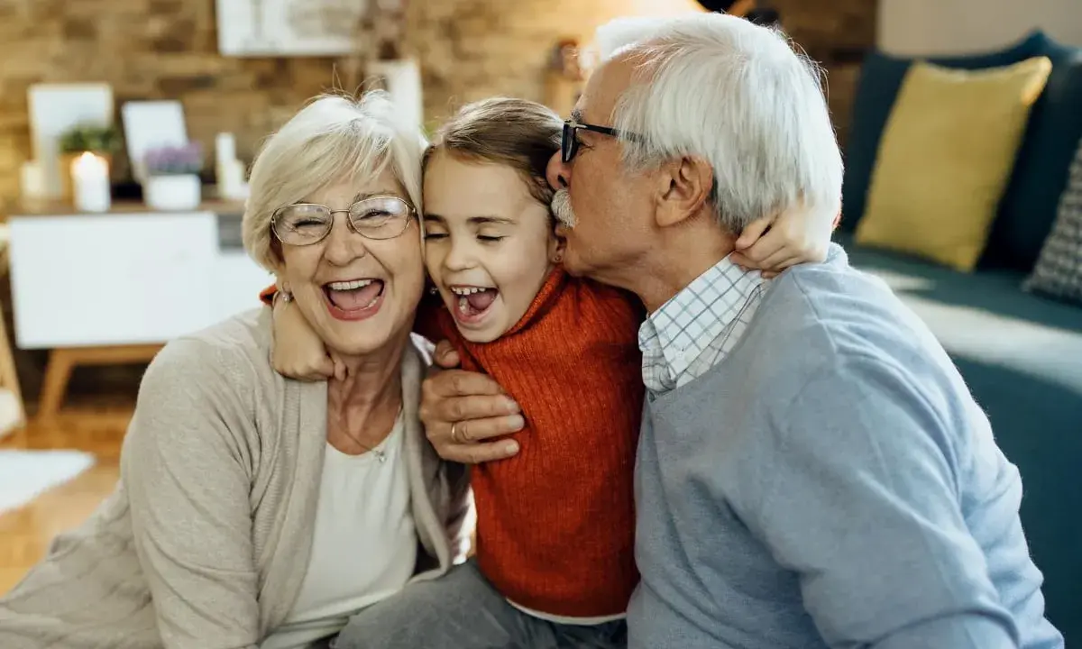 Una niña ríe mientras su abuelo le da un beso y su abuela la abraza. Así de felices los abuelos son.