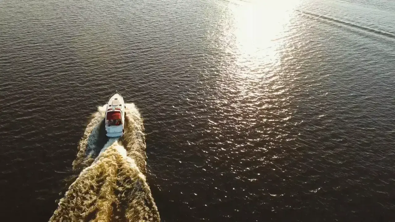 Bateau blanc naviguant sur l'eau sombre, laissant une traînée écumeuse. Le soleil brille, rappelant le temps de séchage Sikaflex.