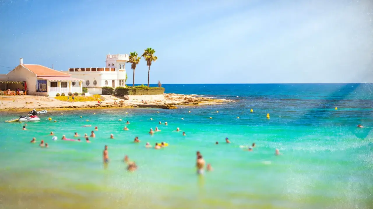 Sonnige Küste in Costa Calida, Spanien, mit vielen Menschen, die im türkisfarbenen Meer schwimmen.