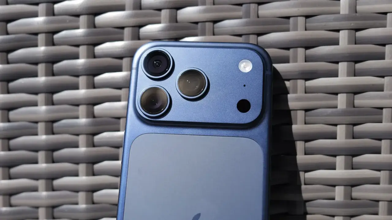 Niebieski iPhone 11 z potrójnym aparatem z tyłu, leżący na plecionej powierzchni.
