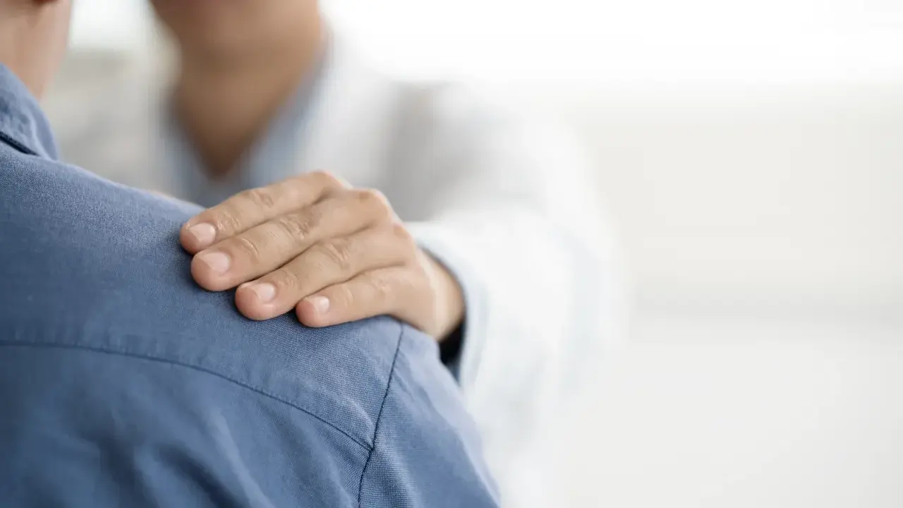 Dłoń lekarza na ramieniu pacjenta. Czy do psychiatry potrzebne jest skierowanie? Wsparcie i troska w gabinecie lekarskim.
