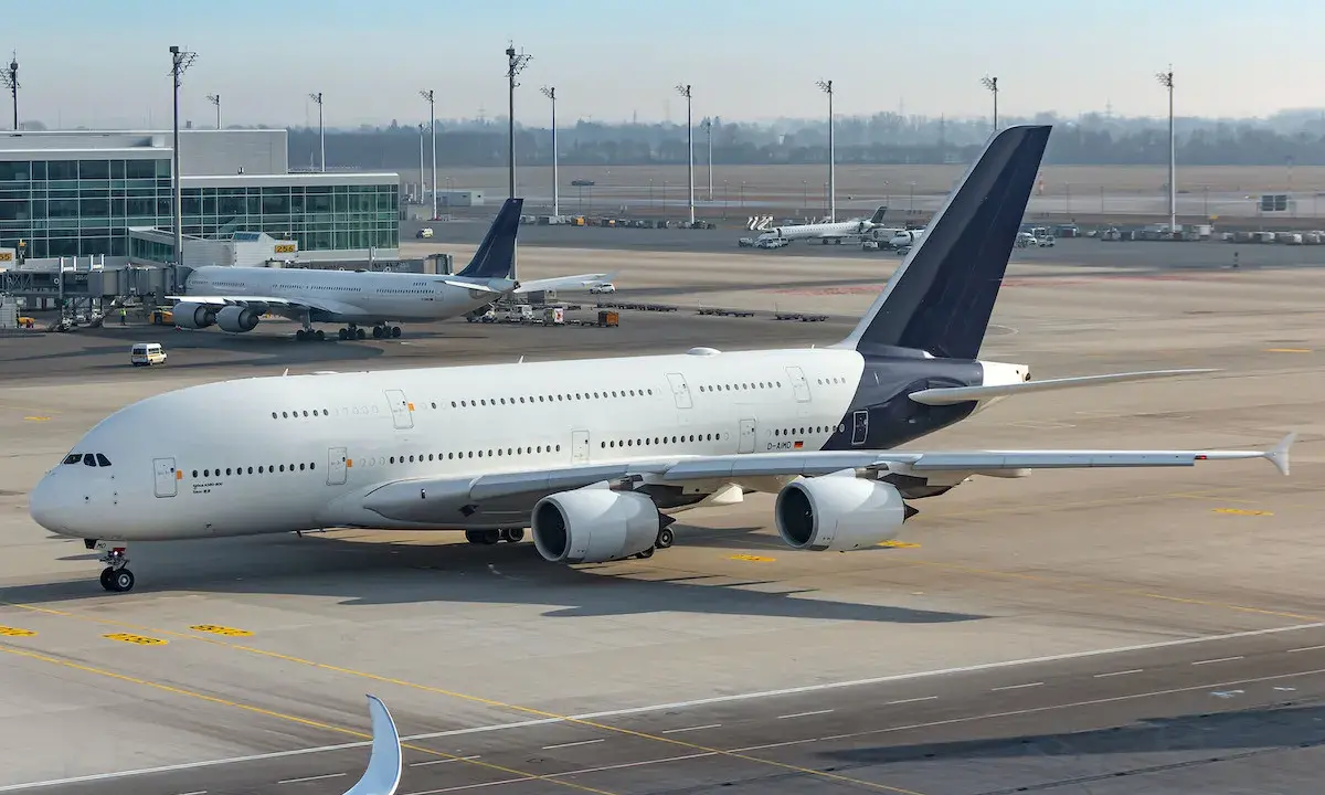 Samolot Airbus A380 na lotnisku, w tle inne samoloty i terminal. Cisza na płycie lotniska, jakby zapowiadała strajk linii lotniczych.