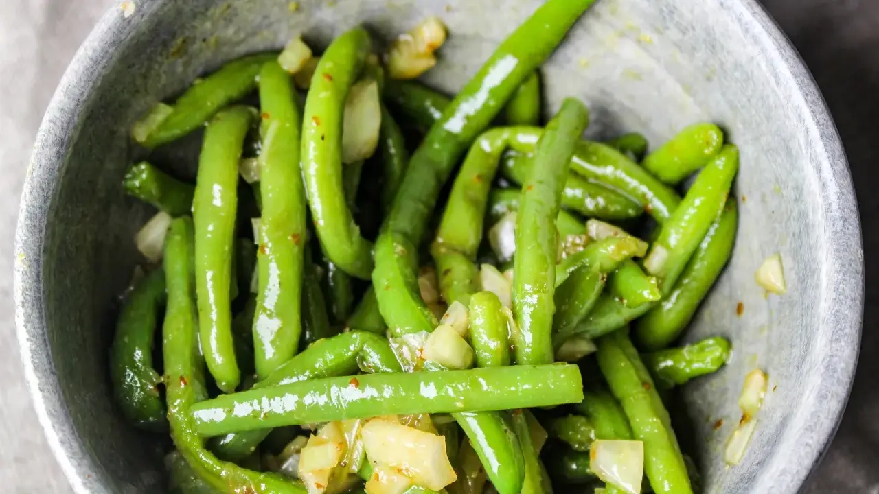 En skål med glansiga, gröna haricots verts blandade med bitar av vitlök och kryddor.