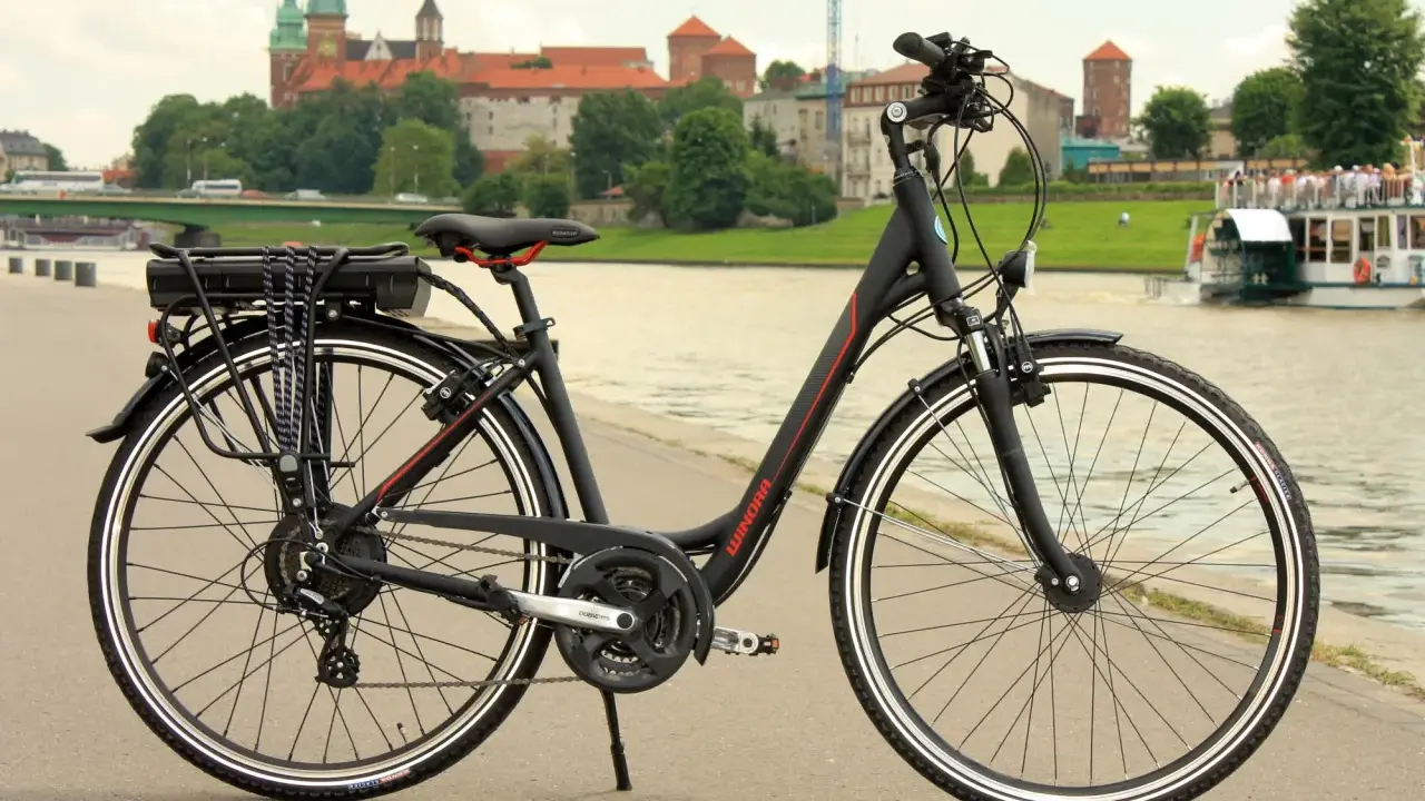 Czarny rower elektryczny z baterią na bagażniku, gotowy do jazdy po bulwarach z widokiem na Wawel.