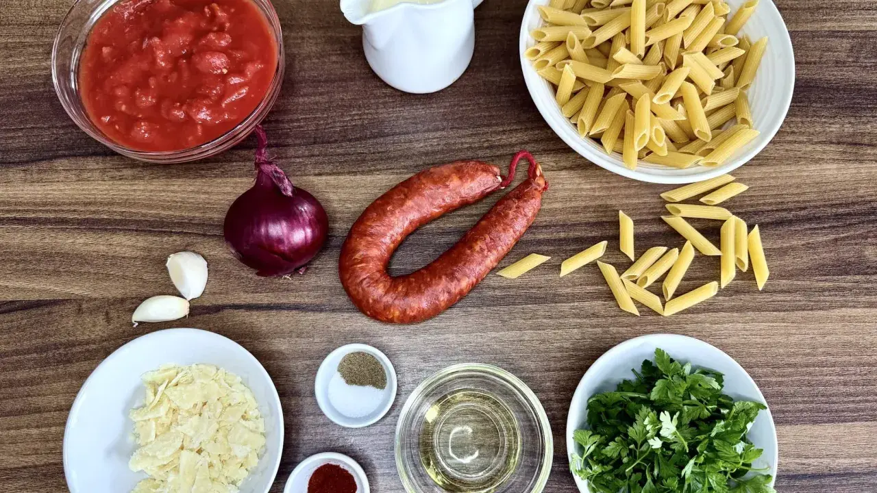 Składniki na pyszny makaron z chorizo: pomidory, cebula, czosnek, makaron penne, śmietanka, parmezan, oliwa, przyprawy i świeża natka pietruszki.